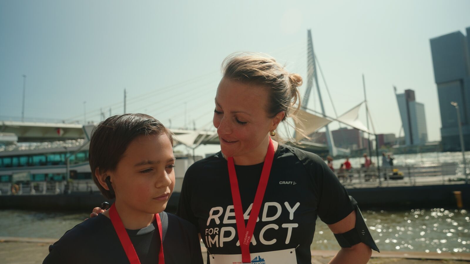 Still uit de aftermovie — moeder en kind met medailles aan de kade