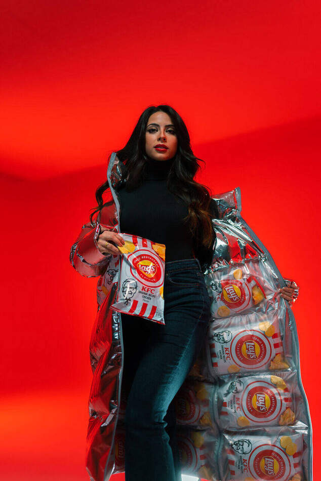 Lay's campagne — model in zilveren pufferjack gevoerd met chipszakken, ten voeten uit op de rode set
