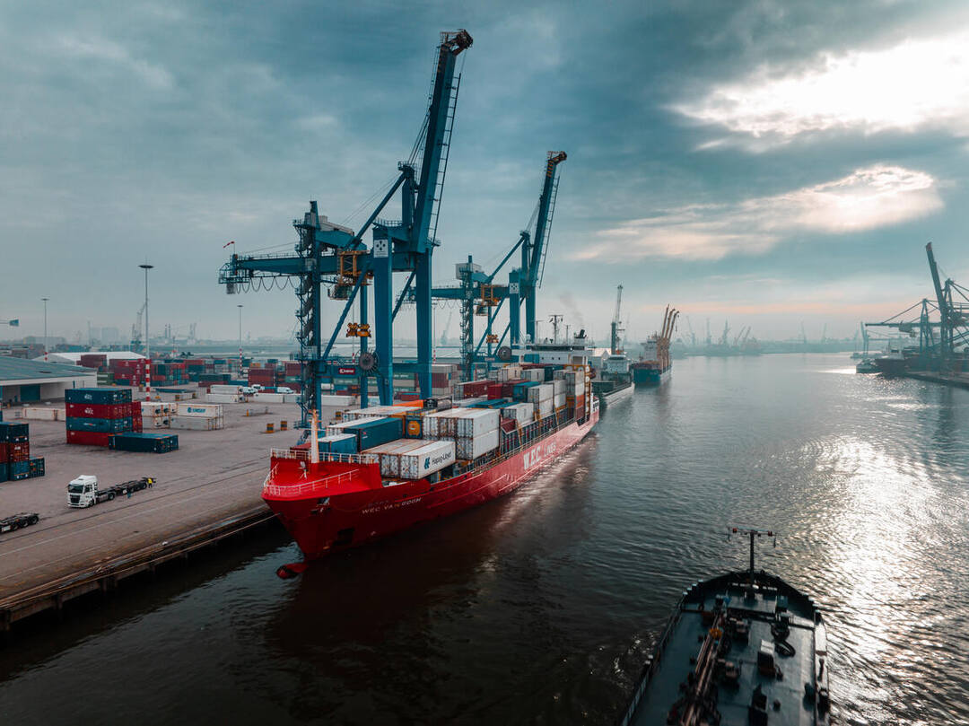 Dronefoto — het rode WEC-schip aan de kade onder een dramatische wolkenlucht