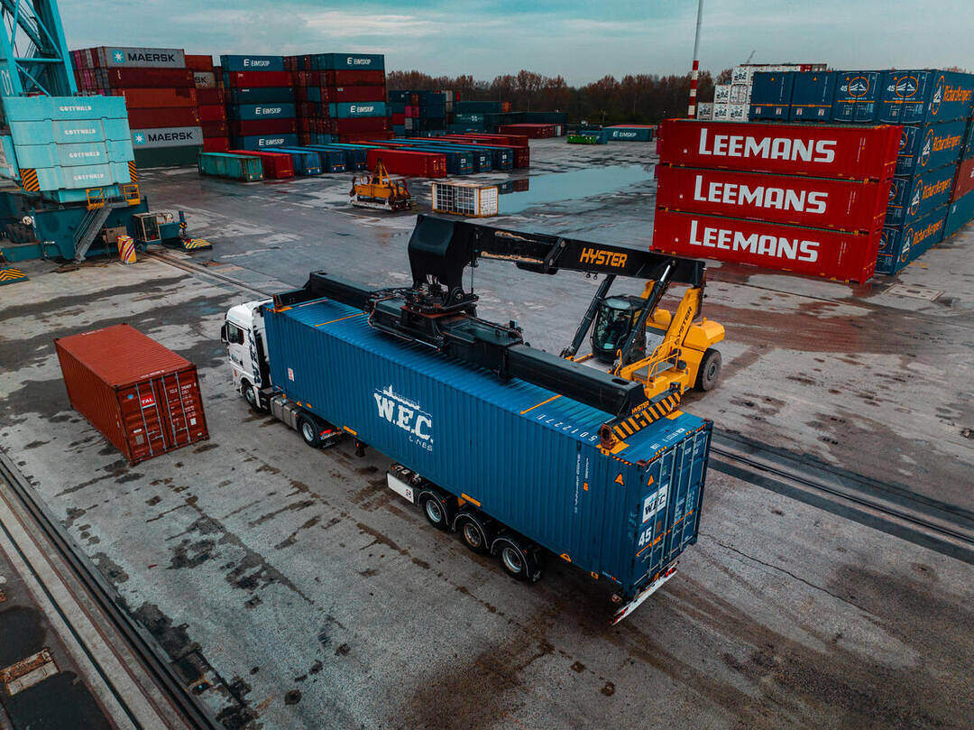 Dronefoto — reachstacker tilt een WEC-container op het containerterrein