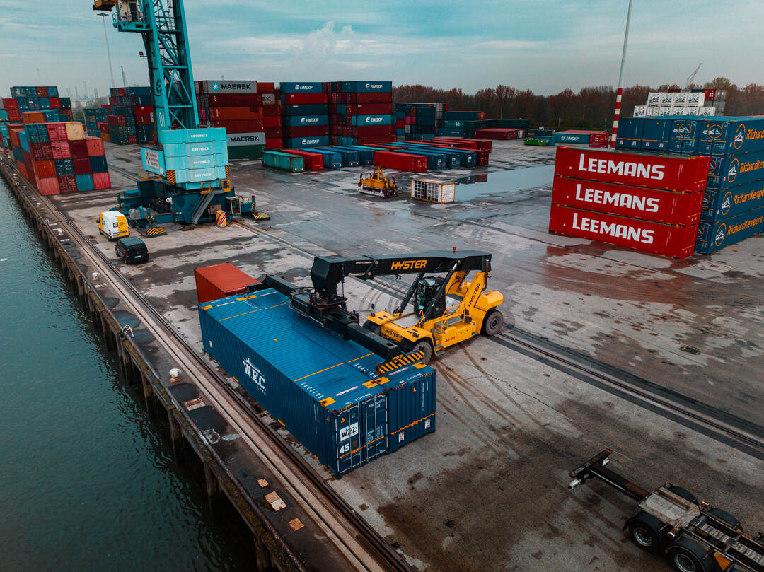 Dronefoto — reachstacker met WEC-container tussen de containerrijen