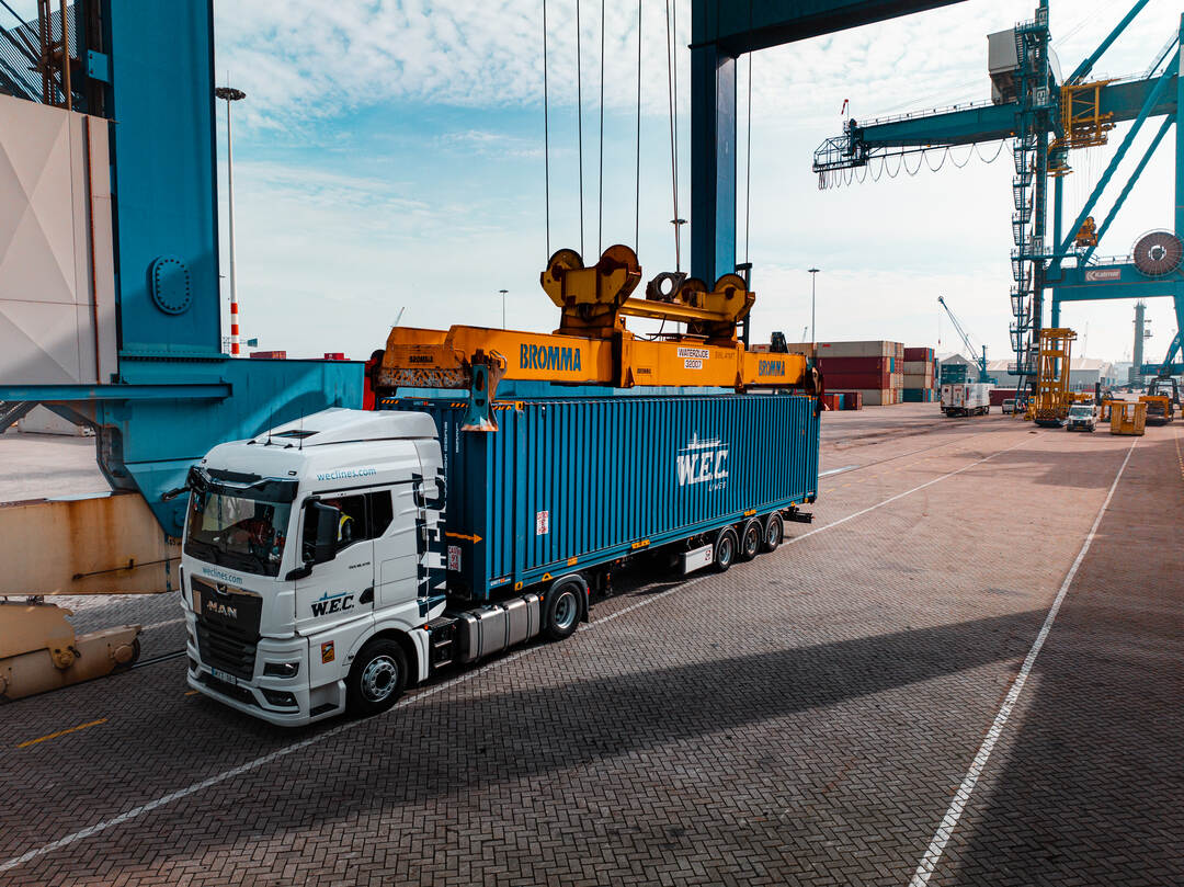 Dronefoto — vrachtwagen met container onder de containerkraan