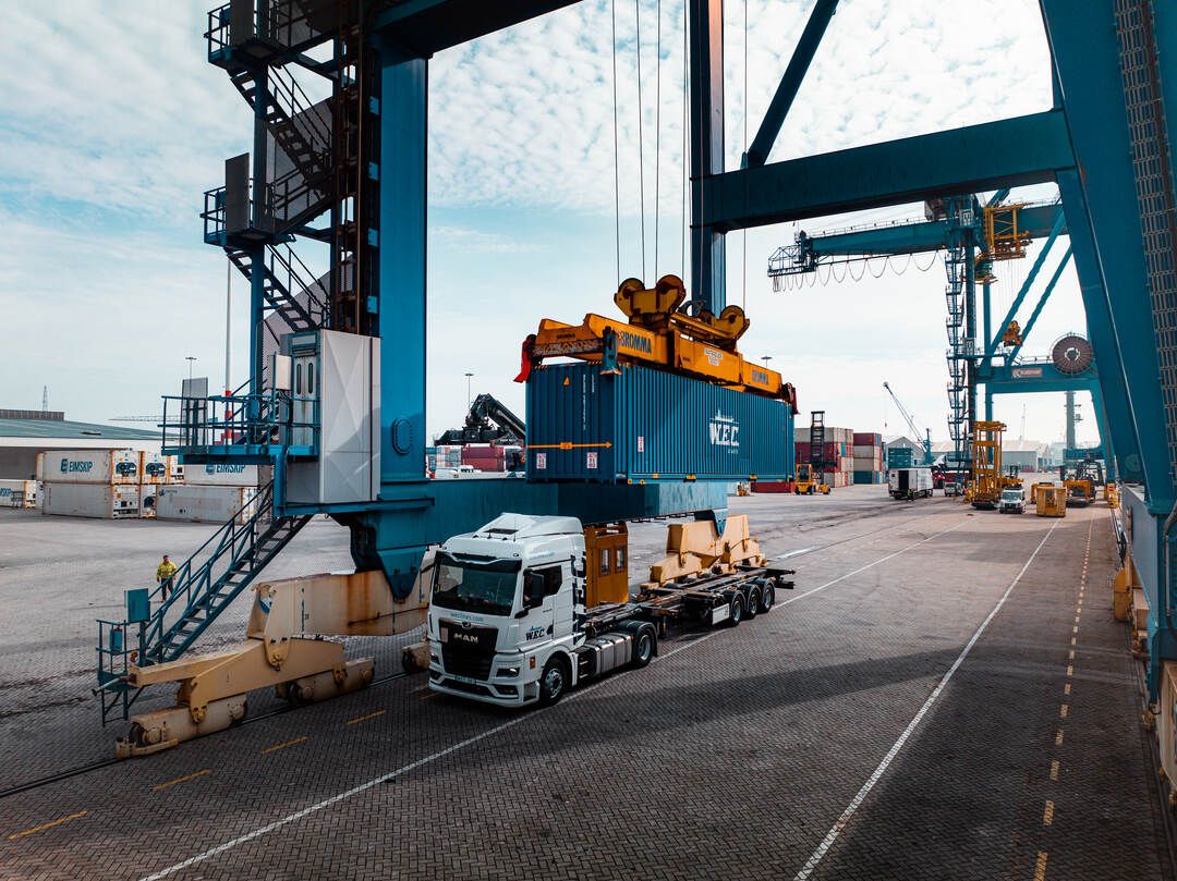 Dronefoto — container hangend aan de kraan boven de kade